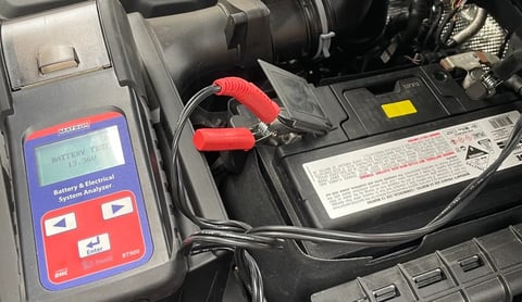Battery tester device with red and black clamps connected to a car engine battery for diagnostics