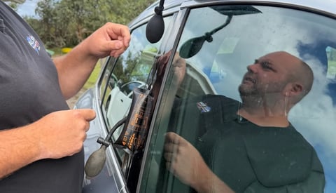 A technician adjusts a cars windshield wiper blade while another person observes from inside the vehicle